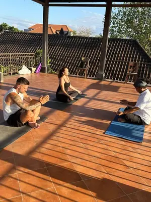 a group of people sitting on mats on a deck at Bali Telaga Hati Yoga Healing And Retreat Center Hostel in Sanur