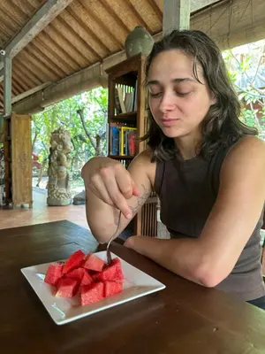 a woman cutting up a piece of fruit on a plate at Bali Telaga Hati Yoga Healing And Retreat Center Hostel in Sanur