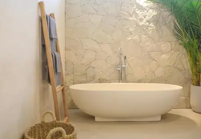 a white bath tub in a bathroom with a stone wall at Villa Isea-3 bedroom with pool in Seminyak