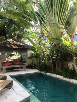 a swimming pool in a garden with a bench and palm trees at W villa in Seminyak