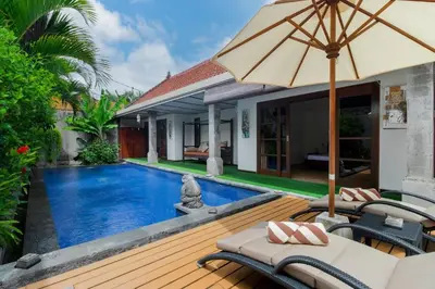 a pool with chairs and an umbrella next to a house at Villa Tranquil Holiday Villa in Seminyak