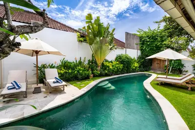 a swimming pool in a backyard with chairs and an umbrella at Villa Amsa by Pertama Management in Seminyak