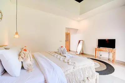 a white bed in a room with a tv at Villa O'Anne in Seminyak