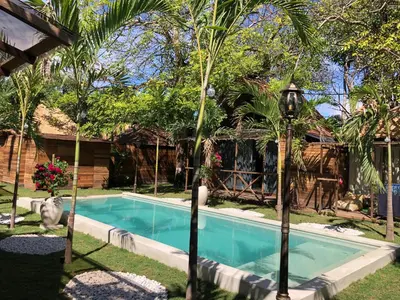 a pool with palm trees in front of a house at Bali Cozy Bungalows, Nusa Dua Benoa in Nusa Dua