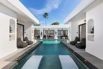 an infinity pool in a villa with chairs and a house at Villa Kelolyne in Seminyak