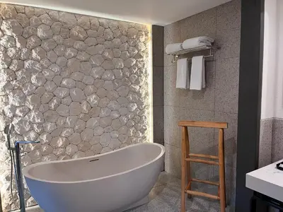a bath tub in a bathroom with a stone wall at Luminor Hotel Legian Seminyak - Bali in Legian