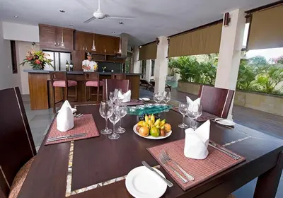a dining table with a bowl of fruit and wine glasses at Barimantra 4BR Trees View Pool Villa CYN in Jimbaran