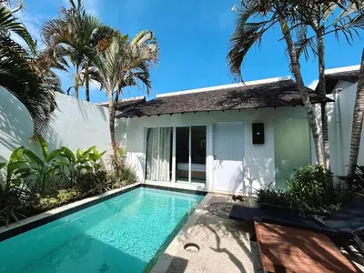 a swimming pool in front of a house with palm trees at Astana Villas in Seminyak