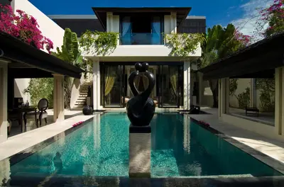 a pool with a statue in front of a house at Villa One Seminyak in Seminyak