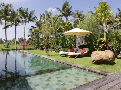 a swimming pool with an umbrella and chairs next to a resort at Dea Villas in Canggu