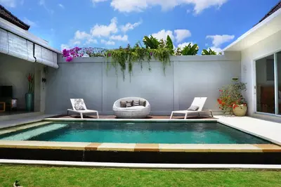 a swimming pool in a backyard with two chairs at Villa Angela in Seminyak