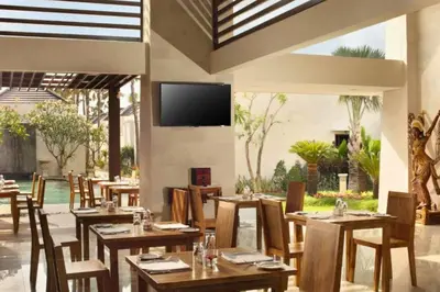 a restaurant with wooden tables and chairs and a flat screen tv at Vadjar 1 BR Private Pool Villa in Seminyak