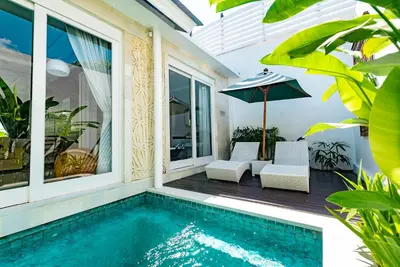 a swimming pool with two chairs and an umbrella at Bajra Bali Villa Seminyak in Seminyak