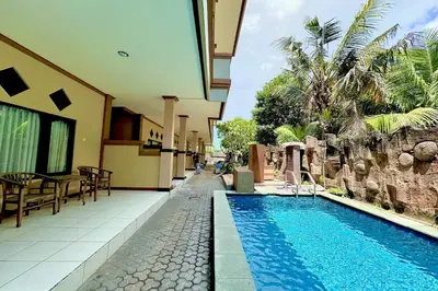 a swimming pool next to a building with a resort at Taxa Raya Guest House in Legian