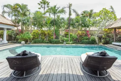 a swimming pool with two chairs next to a wooden deck at Villa Bliss a Paradise of Three Independent Villas in Canggu