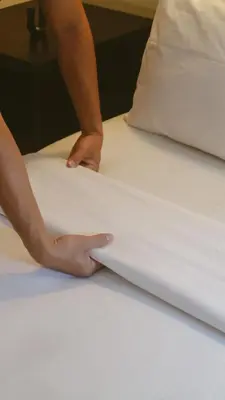 a person is putting sheets on a bed at New Puri Asih Hotel in Kuta
