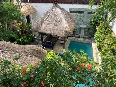a person sitting under an umbrella next to a pool at Villa Petra Seminyak Bali in Seminyak