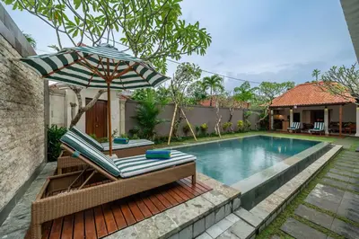 a pool with a chair and an umbrella next to a swimming pool at Villa MD 2 Stylish 3 BR w/ Sunny Pool at Prime Eat Street in Seminyak
