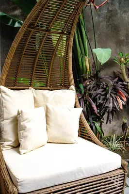 a wicker chair with pillows in front of a plant at Villa Sun Lila by JB Villas in Seminyak