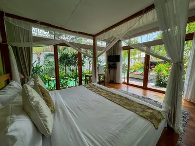a bedroom with a white bed with a large window at Tranquil Classic Balinese Villa in Badung