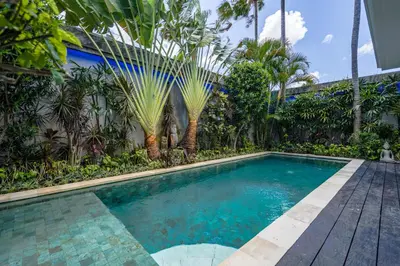 a swimming pool in front of a house with palm trees at Villa Céline 1 Bdr pool Seminyak in Seminyak