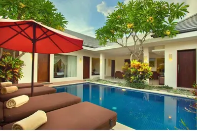 a swimming pool with two chairs and an umbrella at Ageratum 4 BR Villa Private Pool in Seminyak