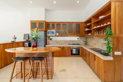 a kitchen with wooden cabinets and a wooden island with bar stools at Villa Ayuni, Berawa in Canggu