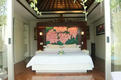a bedroom with a white bed with a painting on the wall at Vlad Bali Villa in Jimbaran