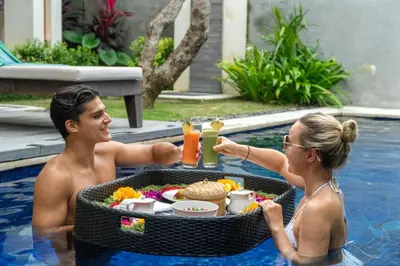 a man and woman sitting in a swimming pool with a tray of food at Ghana Villa Seminyak by GenuineHost in Seminyak