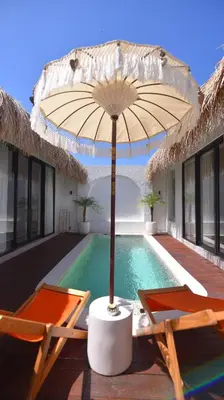 a swimming pool with two chairs and an umbrella at Queen Villa Seminyak in Seminyak