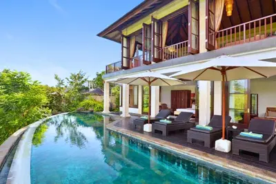 a house with a swimming pool with chairs and umbrellas at Dendalion 4 BR Private Pool Villa in Jimbaran