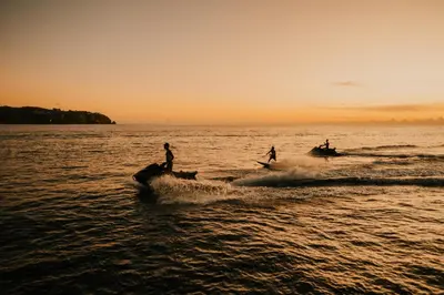 three people on boats in the water at sunset at Floating Hotel SALTWATER COWBOYS in Kuta