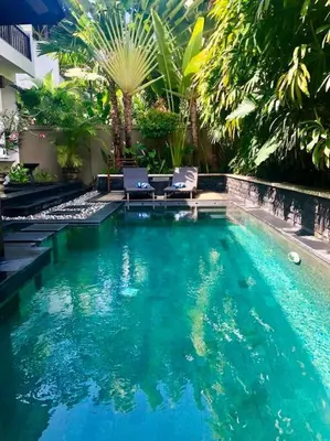 a large swimming pool with two chairs and trees at Villa Teratai in Seminyak