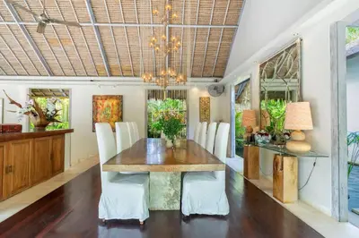 a dining room with a wooden table and white chairs at 4BR Villa with Large Pool at Seminyak Beach in Seminyak