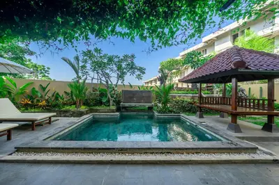 a pool in a courtyard with a bench and an umbrella at Aradhia Villa Nusa Dua in Nusa Dua