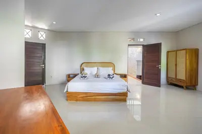 a bedroom with a bed with white sheets and wooden furniture at Aradhia Villa Nusa Dua in Nusa Dua