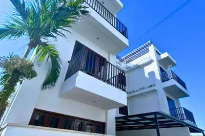 a white building with a palm tree in front of it at Willy 4 BR Comfort Quadruple Room in Jimbaran