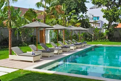 a pool with lounge chairs and umbrellas next to a resort at Nawasena 5 BR Private Pool Villa in Canggu