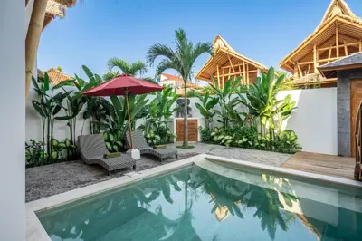 a pool with chairs and an umbrella next to a house at The Secret Jungle Villas Seminyak in Seminyak