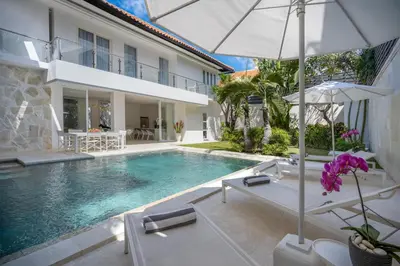 a swimming pool with chairs and an umbrella and a house at Villa Manis Cantik in Seminyak