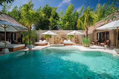 a swimming pool with palm trees and umbrellas at Villa Coconut Heaven by Bali Villa Solutions in Seminyak
