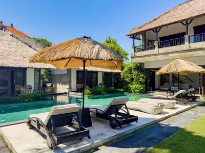 a pool with chairs and umbrellas next to a house at Villa Blubambu in Seminyak