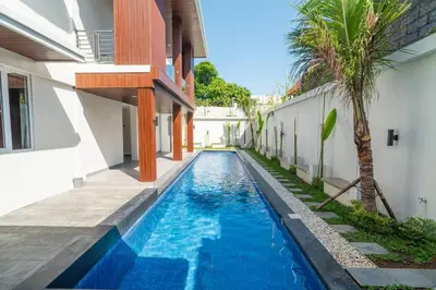 a swimming pool next to a house with a palm tree at Alyxia 1 Bedroom Apartment in Central Seminyak in Seminyak