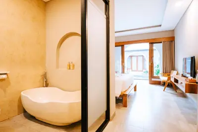 a bathroom with a bath tub and a bedroom at Villa Koura Kuta in Kuta