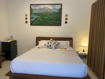 a bedroom with a white bed with a painting on the wall at Manis Guest House in Seminyak