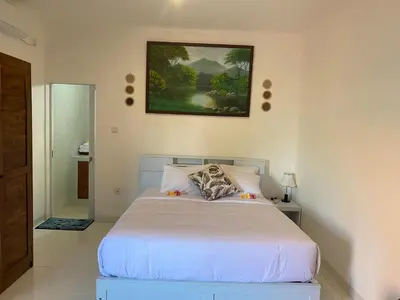 a bedroom with a white bed and a painting on the wall at Manis Guest House in Seminyak