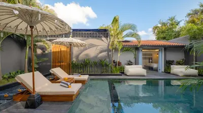 a pool with chairs and an umbrella next to a house at Villa Alami by Villa Finder in Seminyak
