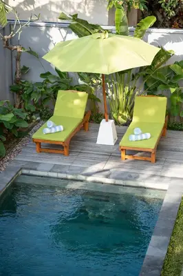 two chairs and an umbrella next to a pool at Titeng Guest House - Comfortable studio in amazing location near Potato Head and the beach in Seminyak