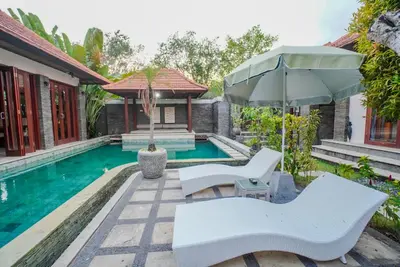 a pool with two white chairs and an umbrella at Villa Di Bucu, Canggu in Canggu