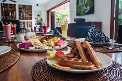 a table with plates of waffles and fruit on it at Villa Annecy in Seminyak